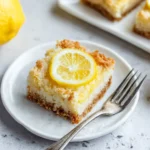 Single lemon coconut bar on a white plate, garnished with a lemon slice and fork on the side | kaynmaytkal.com